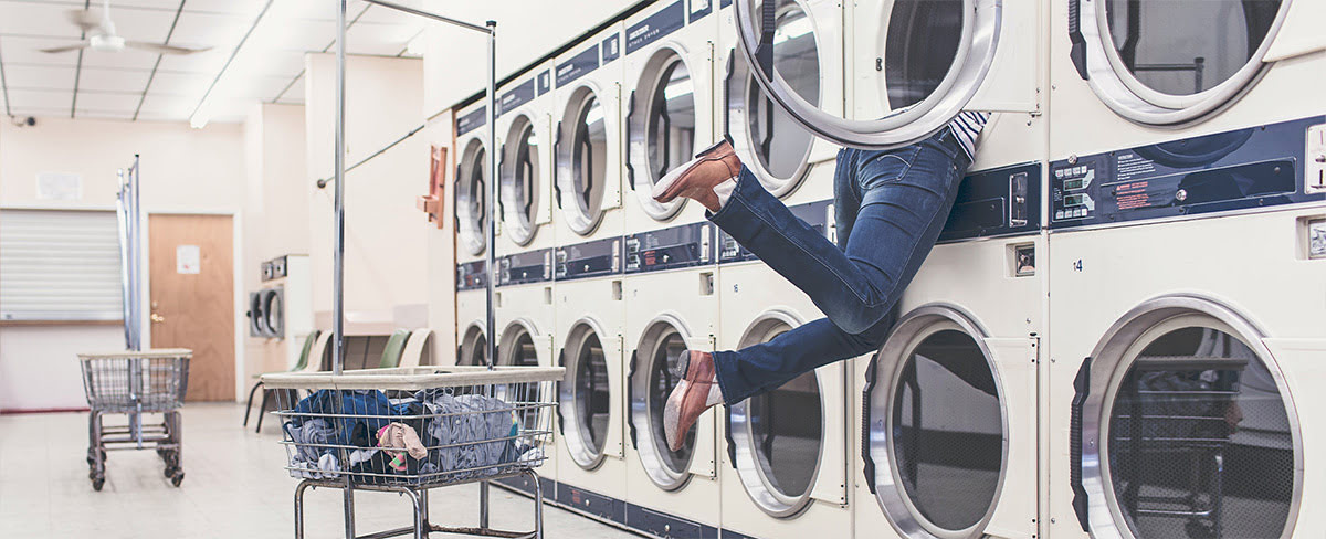 A pair of legs hanging out a washing machine in a laundrette