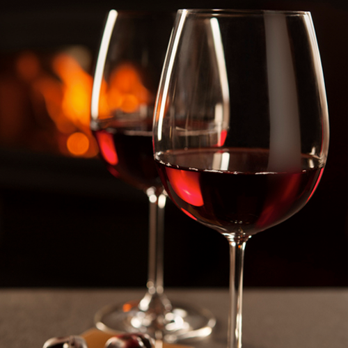 Two wine glasses half full with red wine in front of a fire